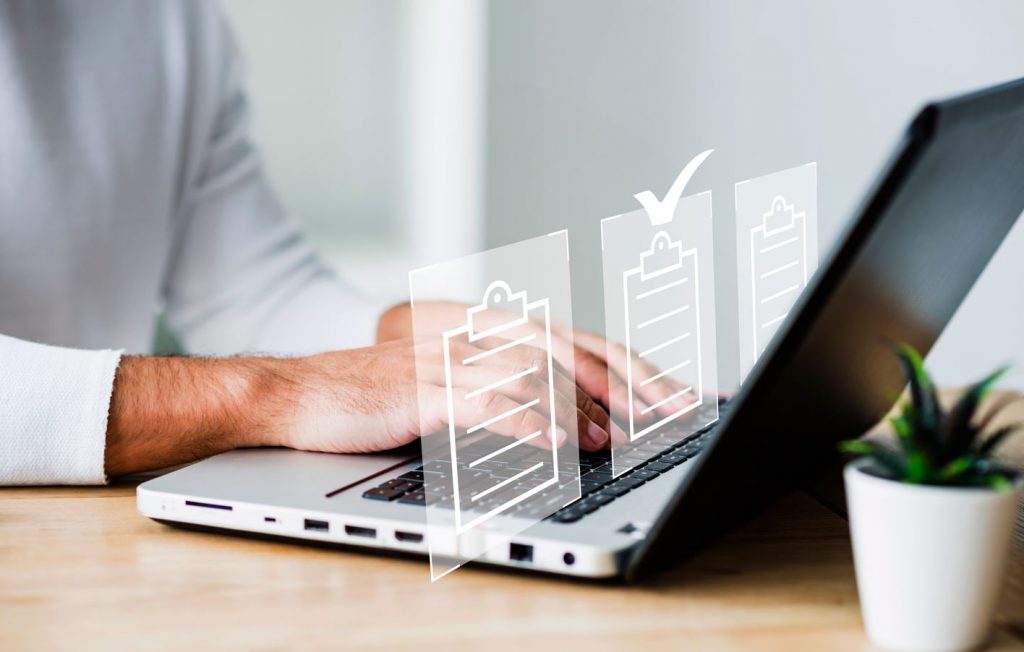 Foco nas mãos de um homem utilizando um notebook. À frente da tela, aparecem projeções virtuais que simboliza documentos digitais